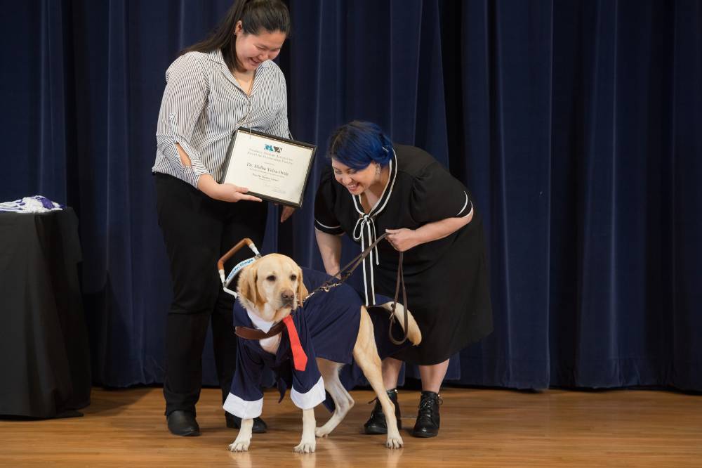 GSA Presient and Professor smiling at the Professor's service dog, who is dressed in a suit for the event